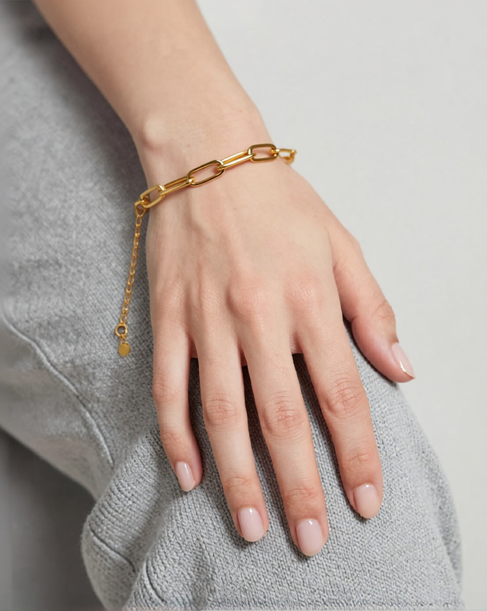 Gold paperclip chain bracelet worn on the wrist of a model with fair skin