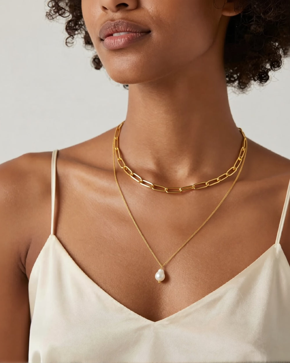 Layered gold chain necklace with a single pearl worn on deep brown skin