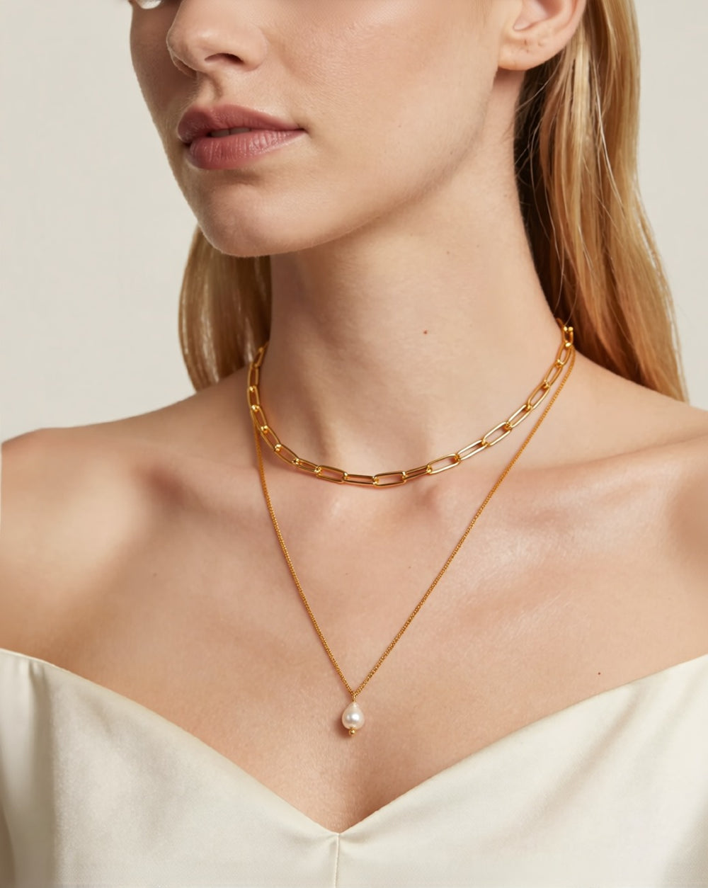 Double-layer gold paperclip chain necklace with a pearl drop worn by a model